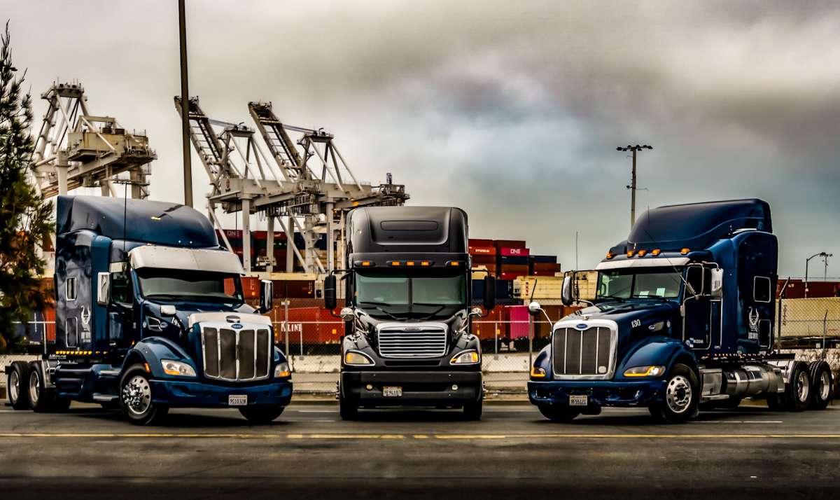 Three tractor-trailer cabs sit parked in a semi-circle at the Port of Oakland.